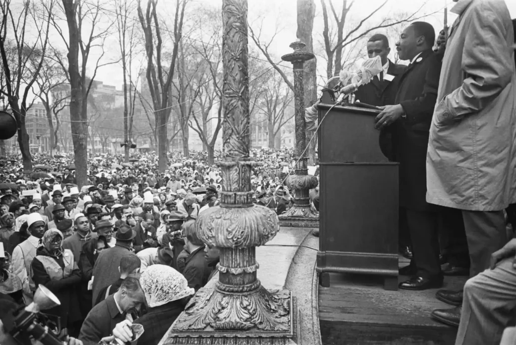Dr. Martin Luther King saying a speech at a podium to a large crowd.